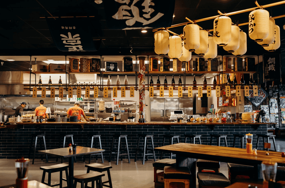 A restaurant interior decorated with Japanese artwork and lanterns, and black tiles on an open kitchen bar.