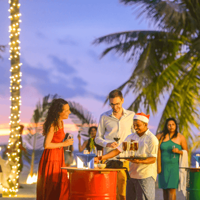 Guests enjoying a festive beachside celebration with string lights and palm trees at twilight