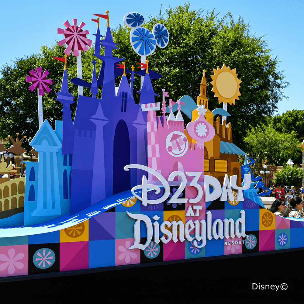 Colorful D23 Day parade float featuring stylized castle facades and decorative pinwheels under a bright sunny sky.