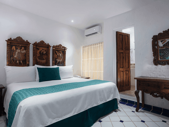 Bed with teal runner below three colonial paintings next to a wooden vanity desk in Standard Jr. Suite at Casa Dona Susana