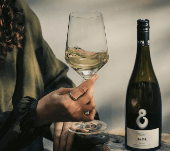 A hand holding a wine glass filled with wine beside a bottle labeled te Pā served at The Okura Prestige Bangkok
