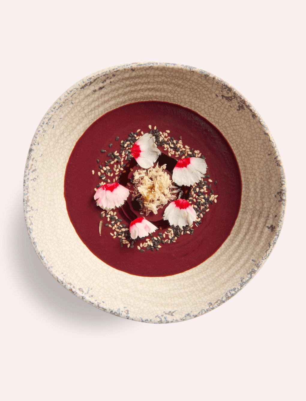 Bowl of deep red soup garnished with edible flowers, sesame seeds and a contrasting topping served at The Londoner Hotel