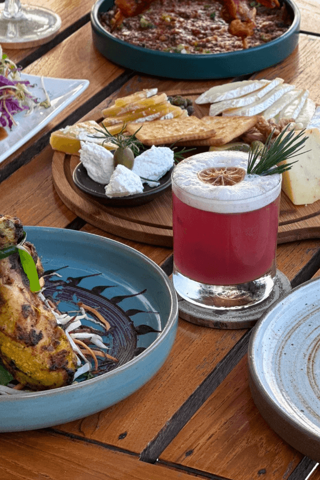 Assorted dishes and a cocktail served on a wooden table in The Terraces Restaurant at The Terraces Resort & Spa