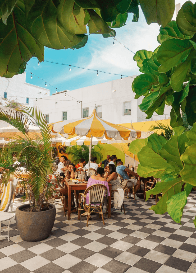 A group of people sitting at tables under yellow and white umbrellas in an outdoor dining area.