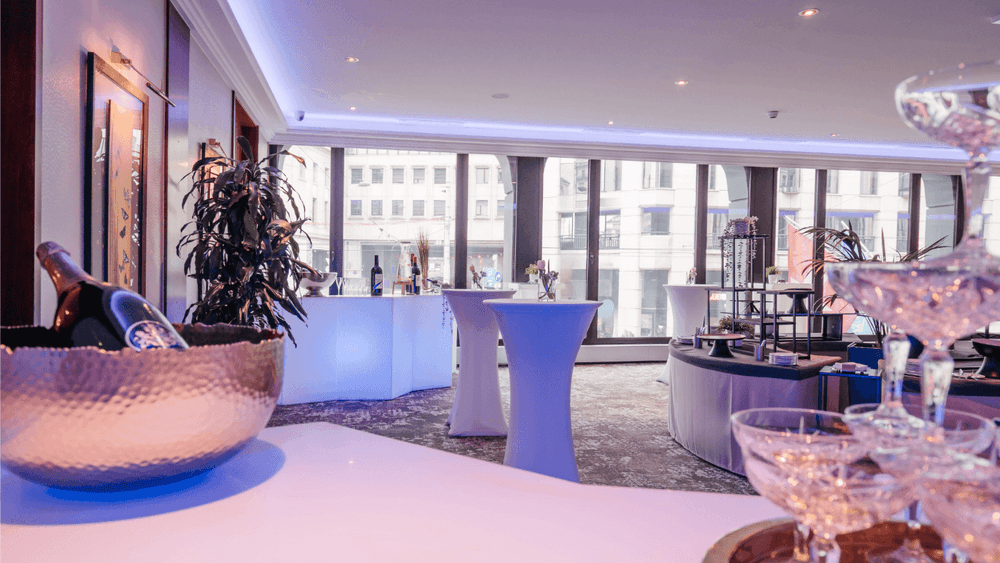 Sleek cocktail tables by large windows under a blue neon glow in Foyer Mezzanine at Warwick Geneva