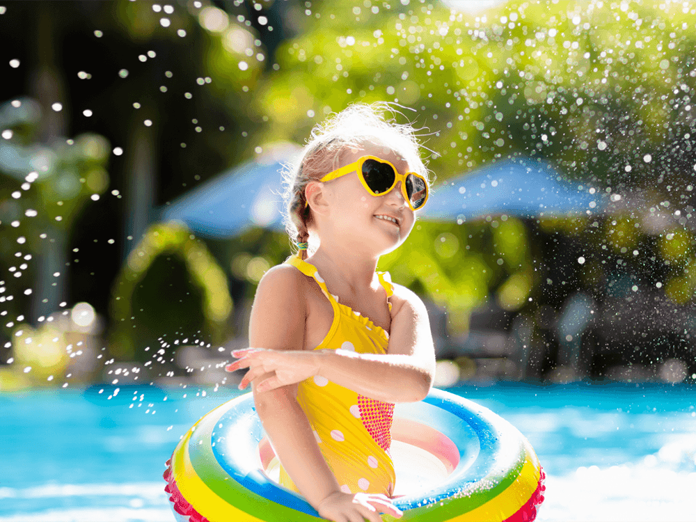 A little girl in a yellow swimsuit & sunglasses having fun in an outdoor pool at Juniper Hill Inn