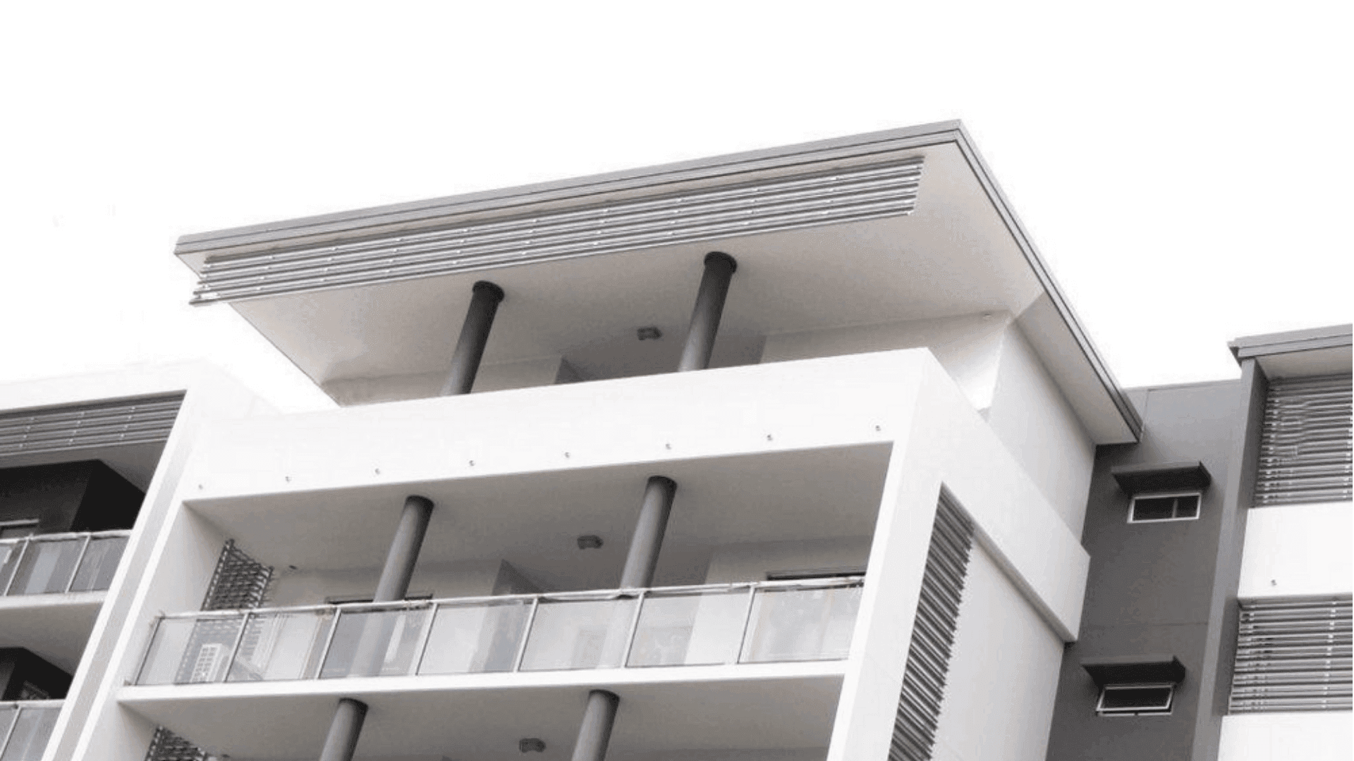 Modern white multi-story building with horizontal louvers and black cylindrical columns supporting balconies.
