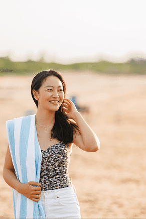 Smiling woman with a blue-striped beach towel on the sand at Rodd Crowbush Golf & Beach Resort