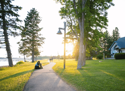 Woman with a dog on a paved walkway during a bright sunset near a lawn by the waterfront grounds at Rodd Brudenell River
