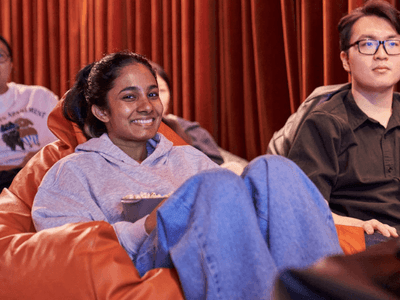 Group of people sitting on beanbag chairs in a cinema, with a woman holding popcorn.