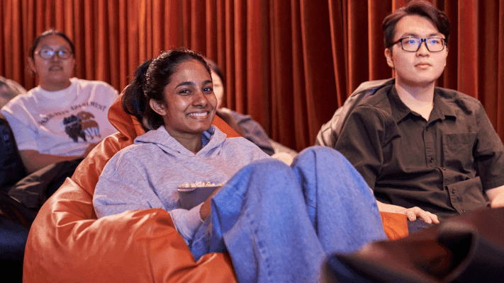 Group of people sitting on beanbag chairs in a cinema, with a woman holding popcorn.