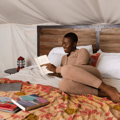 Guest reading a book on a plush bed with a colorful patterned blanket inside a glamping tent at La Tourelle Hotel and Spa