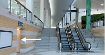 Bright indoor lobby with escalators beside stairs and white arrow pointing towards a doorway located at Hotel X Toronto