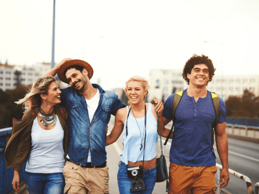 Four travelers with smiles walking together on a bridge for Sizzling Summer Savings.