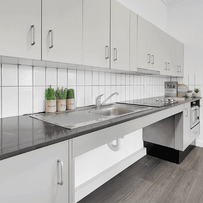 Modern kitchen with white cabinetry, gray countertops, stainless steel sink, and white tile backsplash at Springfield Central.