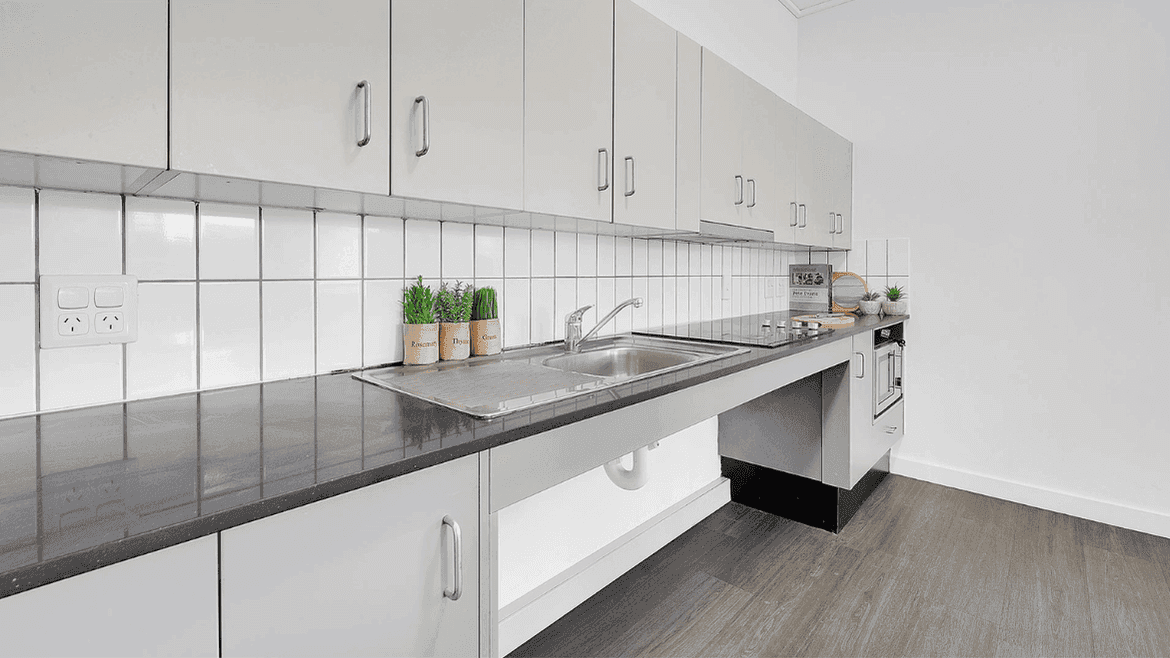 Modern kitchen with white cabinetry, gray countertops, stainless steel sink, and white tile backsplash at Springfield Central.