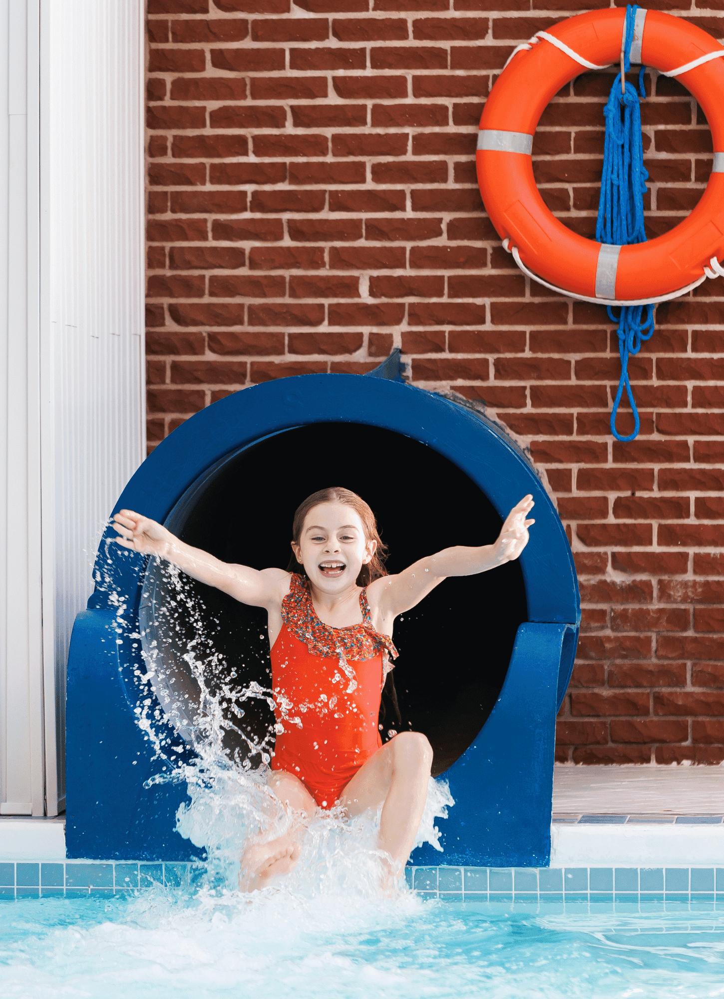 Young girl in a red swimsuit splashing out of a blue pool slide at Rodd Hotels & Resorts