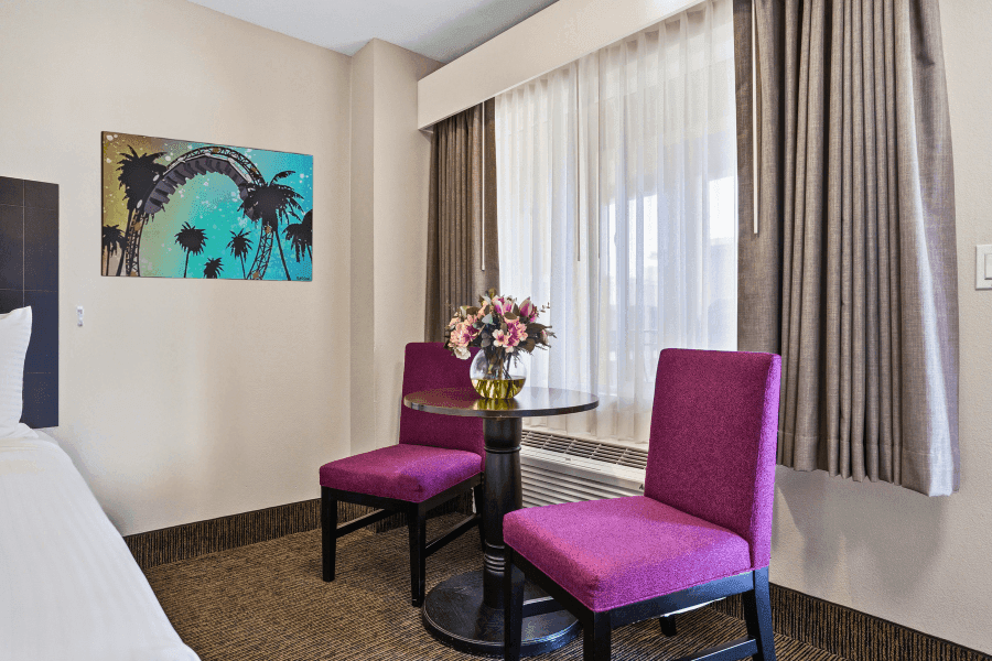 A hotel room with a small table and two purple chairs in front of a window.