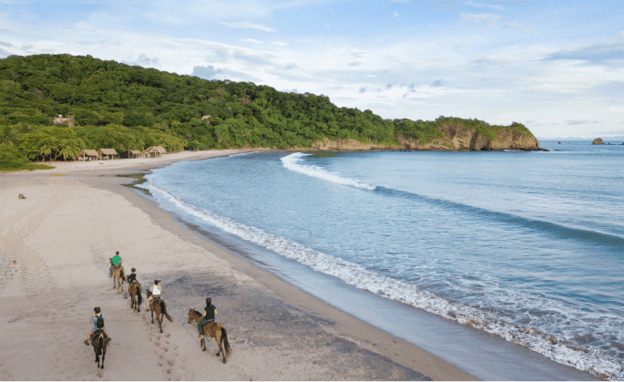 Travelers enjoying a scenic horseback ride along pristine sandy shores at Morgan’s Rock Reserve & Ecolodge