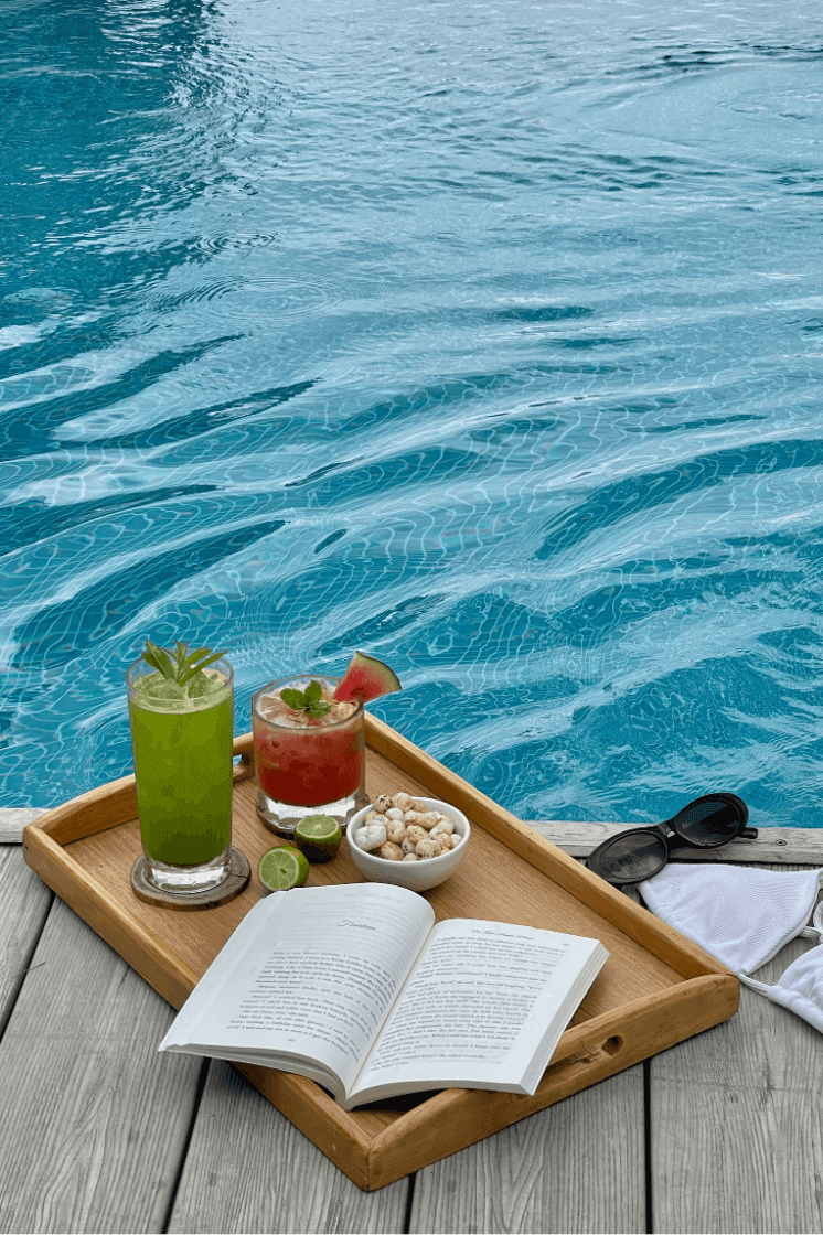 Tray with cocktails and a book by a swimming pool at The Terraces Resort & Spa