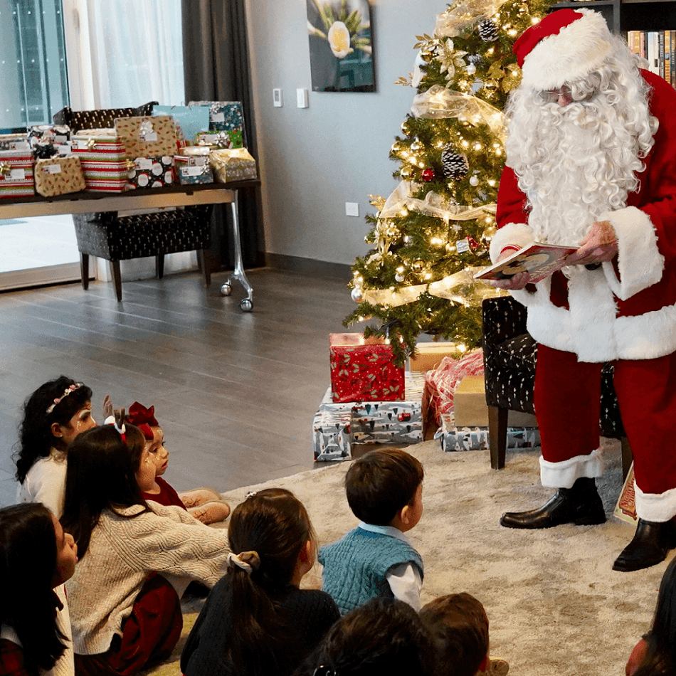 Santa reading to seated children by a lit Christmas tree surrounded by colorful wrapped holiday gifts at Hotel X Toronto