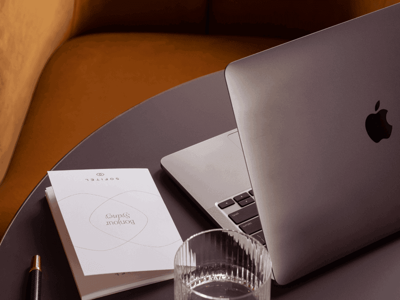 MacBook laptop open on hotel room desk with notebook and warm ambient lighting