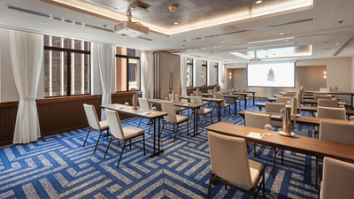 Modern conference room with large screen, tables, chairs, and blue carpet at The Grace Sydney