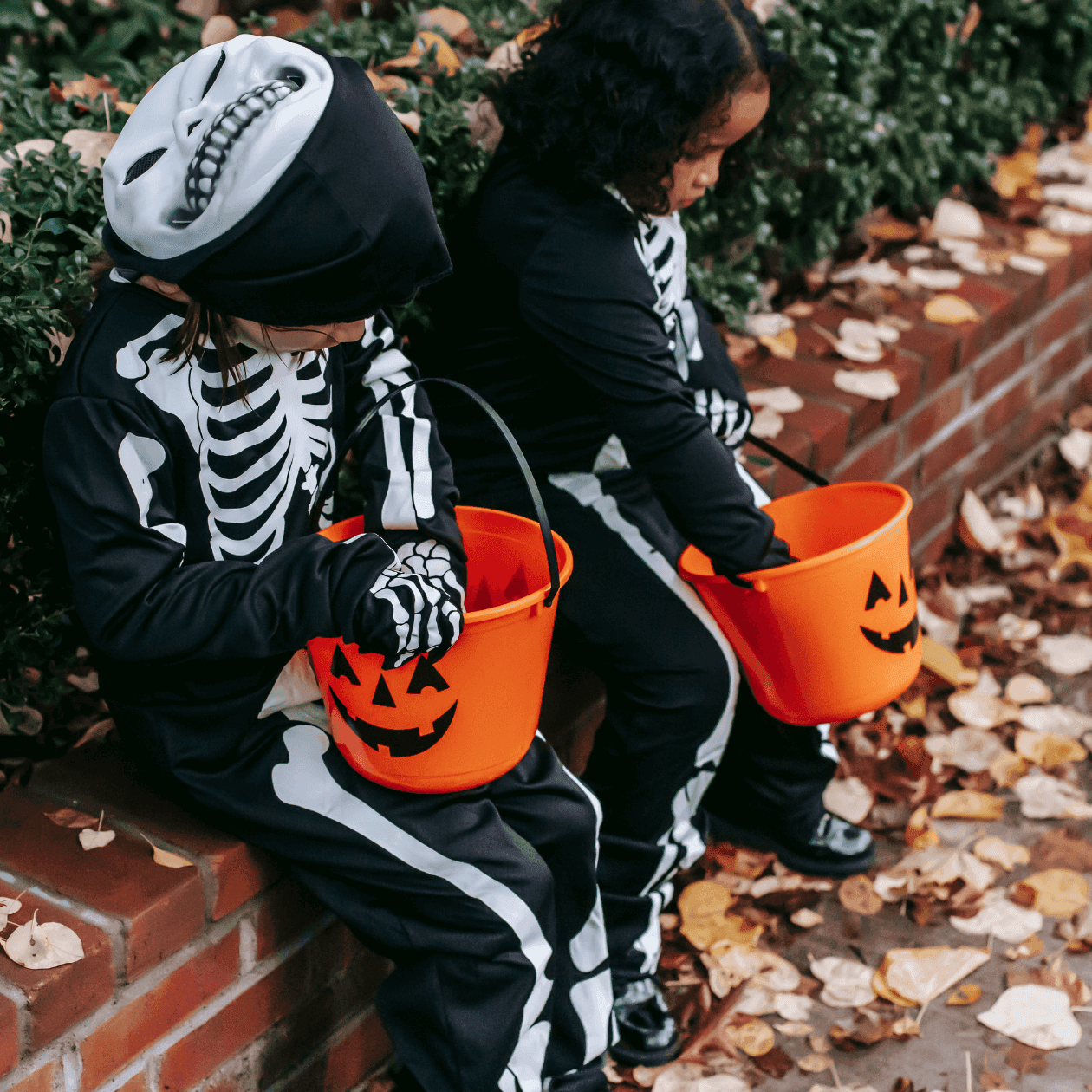 Two children in skeleton costumes sitting on a brick wall holding pumpkin buckets at The Exeter Inn
