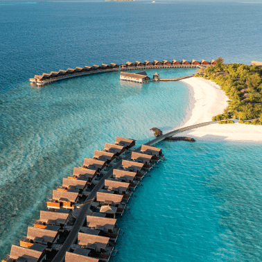 Overwater villas and beach villas along the blue lagoon in an aerial view.