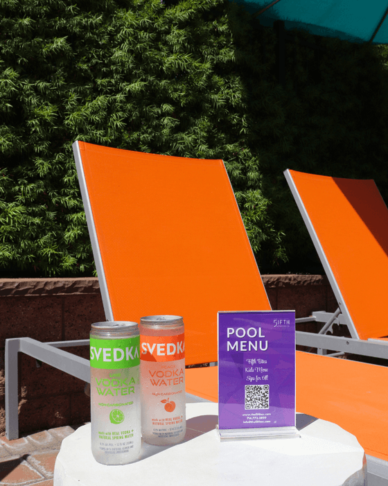 Two drinks and a purple pool menu displayed on a white table beside orange lounge chairs at Grand Legacy at The Park Anaheim