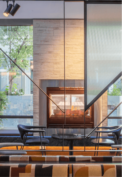 Modern lounge area with a central fireplace, flanked by two chairs and a round table at Amora Herencia Riverwalk Melbourne