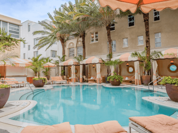 The stylish, curved outdoor pool surrounded by fringed cabanas and lush palm trees at The Plymouth Hotel South Beach