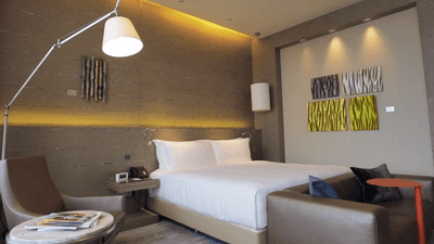 Sleek floor lamp and seating area by the bed in The Skyline Studio bedroom at One Farrer Hotel