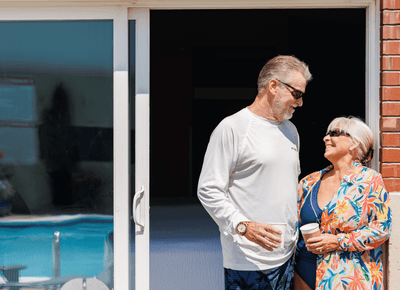 Smiling senior couple holding coffee cups while standing outside a poolside guest room patio entrance at Rodd Moncton