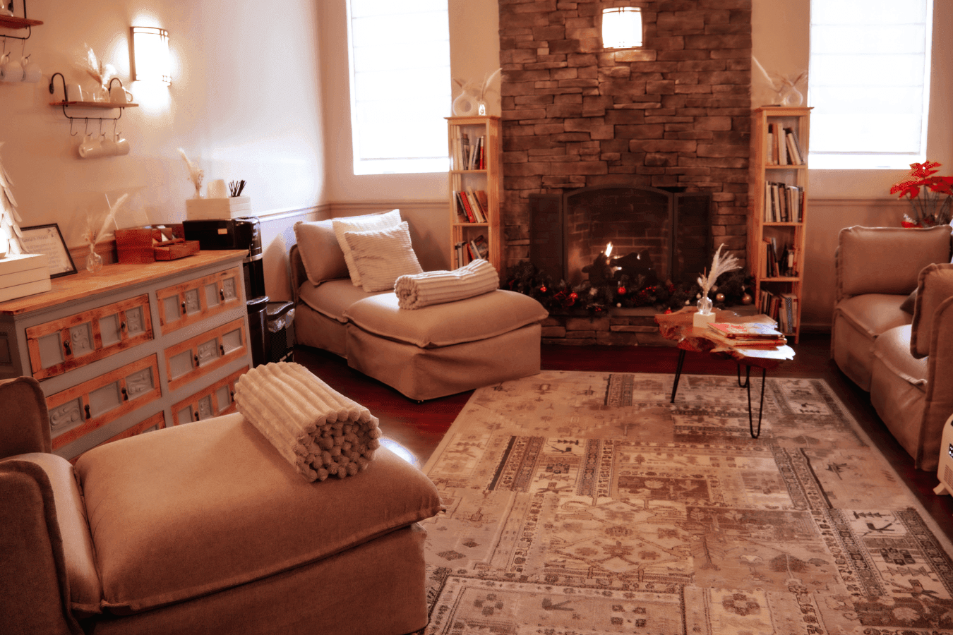 Spa waiting room with cushioned chaise loungers by a stone fireplace and wooden bookshelves at La Tourelle Inn and Spa