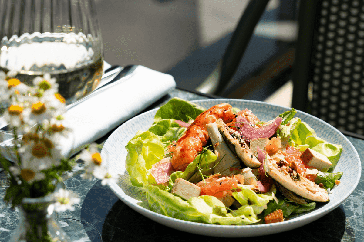 Fresh chicken salad with greens and tomato on a sunlit table at Restaurant, Bar & Terrace Le W, an elite Restaurant in Paris