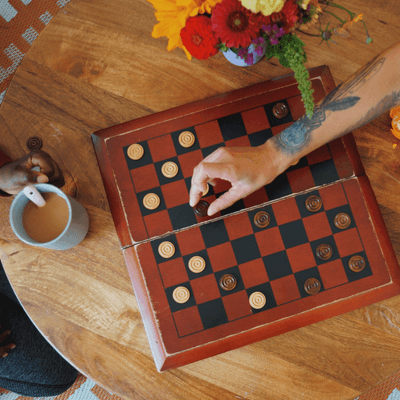 Hands playing a game of checkers on a wooden table beside coffee and fresh flowers at La Tourelle Hotel and Spa