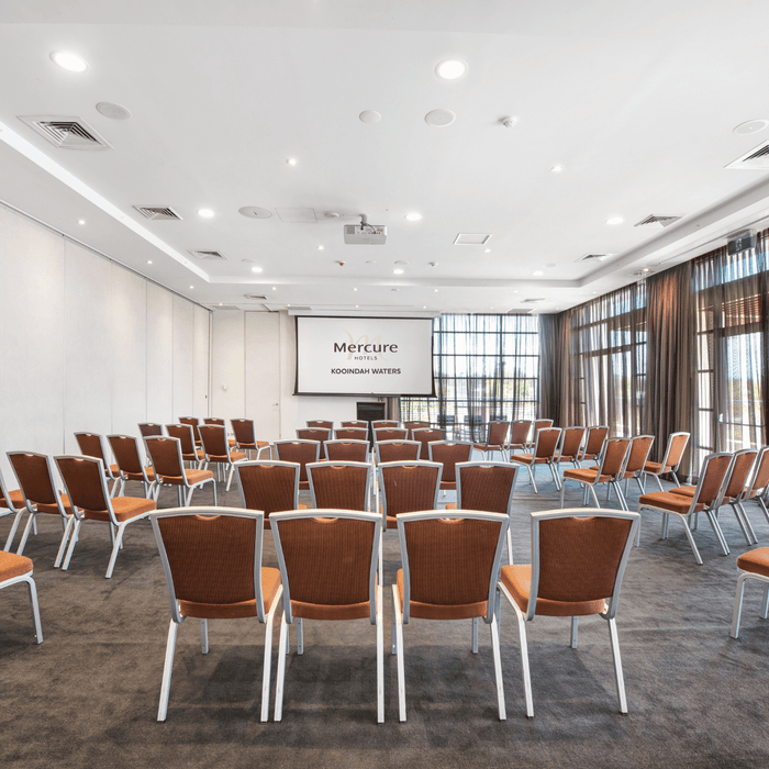 Kooindah One meeting room with rows of orange chairs facing a projector screen at Mercure Kooindah Waters