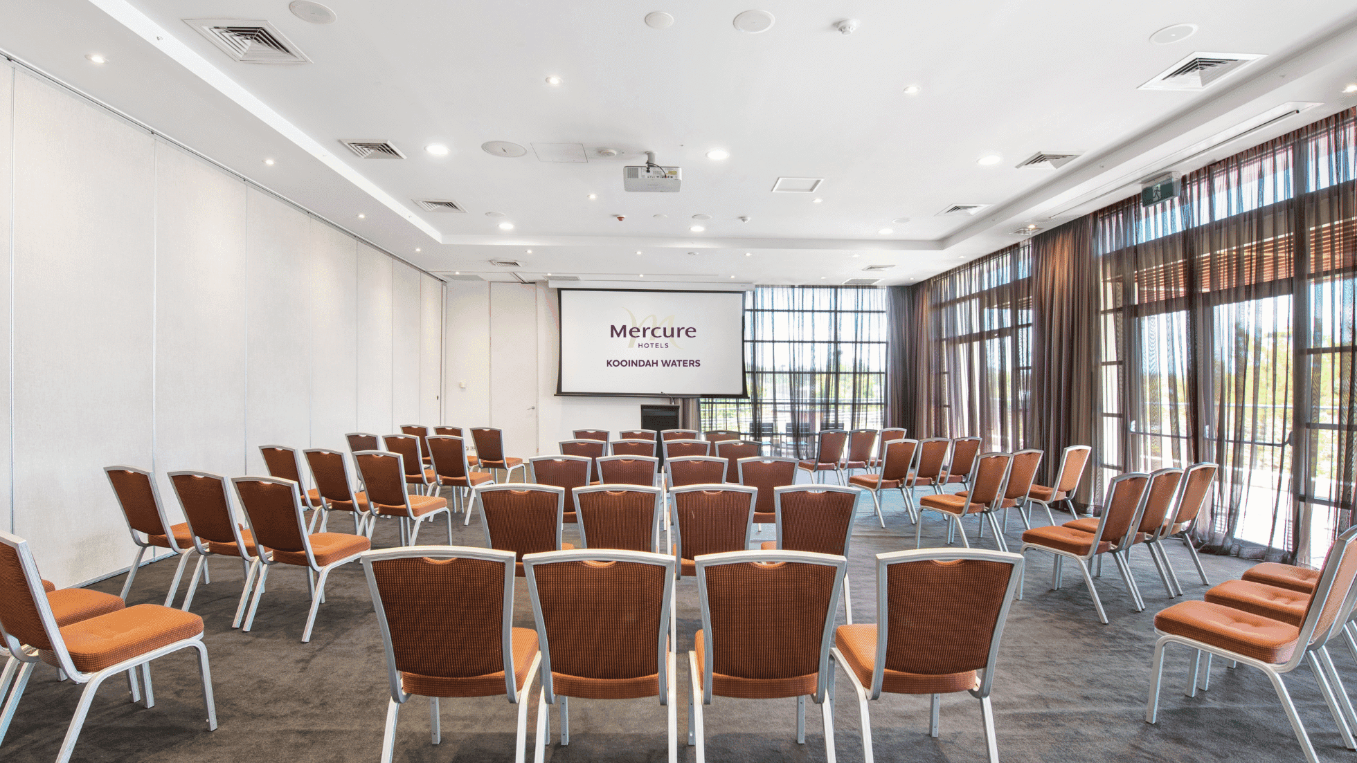 Kooindah One meeting room with rows of orange chairs facing a projector screen at Mercure Kooindah Waters