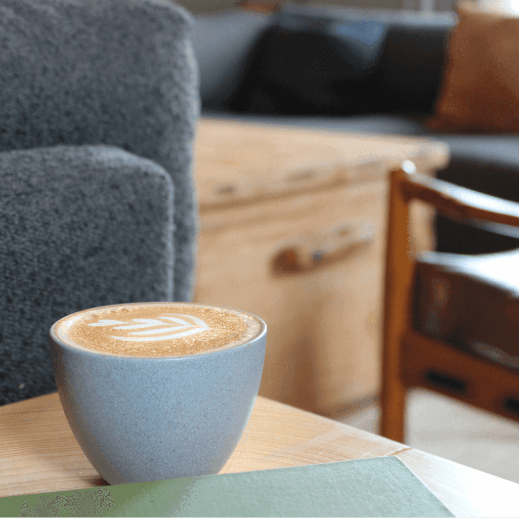 Coffee cup with art on a wooden table surrounded by comfortable seating for Morning Walk & Coffee Social.