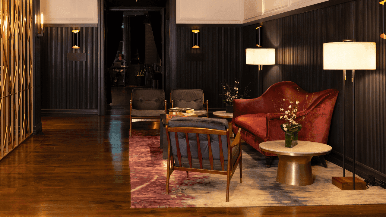 A lobby lounge with a red velvet sofa, wooden chairs, coffee tables, and lamps.
