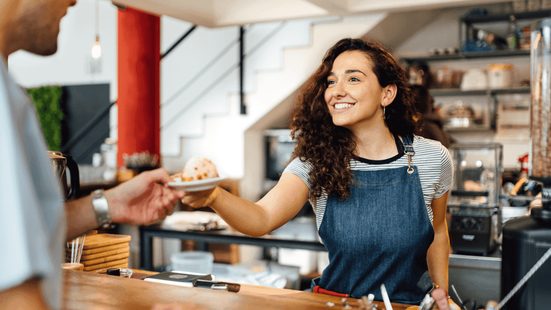 Woman in apron serving a customer with a plate at the counter.