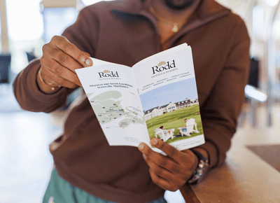 Guest reading a Rodd Hotels & Resorts brochure with property map and resort image at Rodd Crowbush Golf & Beach Resort