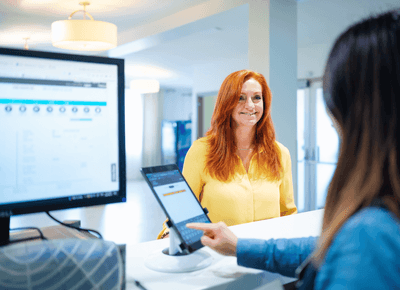 Front desk agent assisting a smiling woman in a yellow blouse at the reception counter check-in area of Rodd Hotels & Resorts
