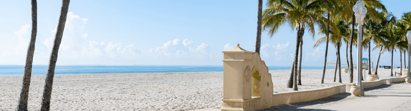 A beach scene with palm trees, a sidewalk, and an ocean view.