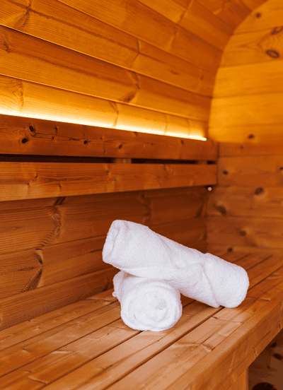 Rolled white bath towels on a cedar bench inside the warm wooden barrel sauna at Rodd Moncton