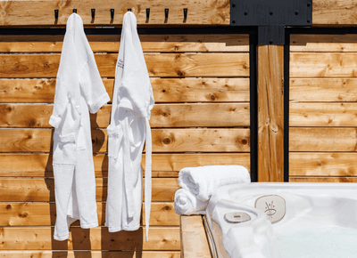 White waffle bathrobes hanging against a wooden privacy wall beside a bubbling outdoor whirlpool hot tub at Rodd Moncton