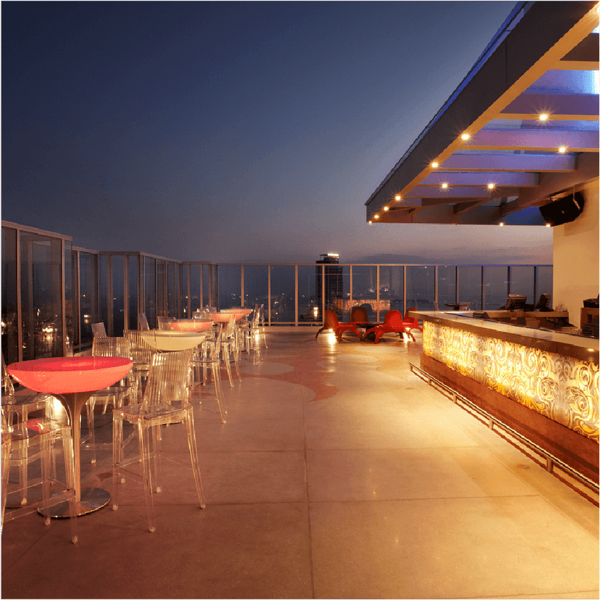 Bar de azotea al atardecer con mesas iluminadas, sillas transparentes y barra acristalada en Megapolis Hotel Panama