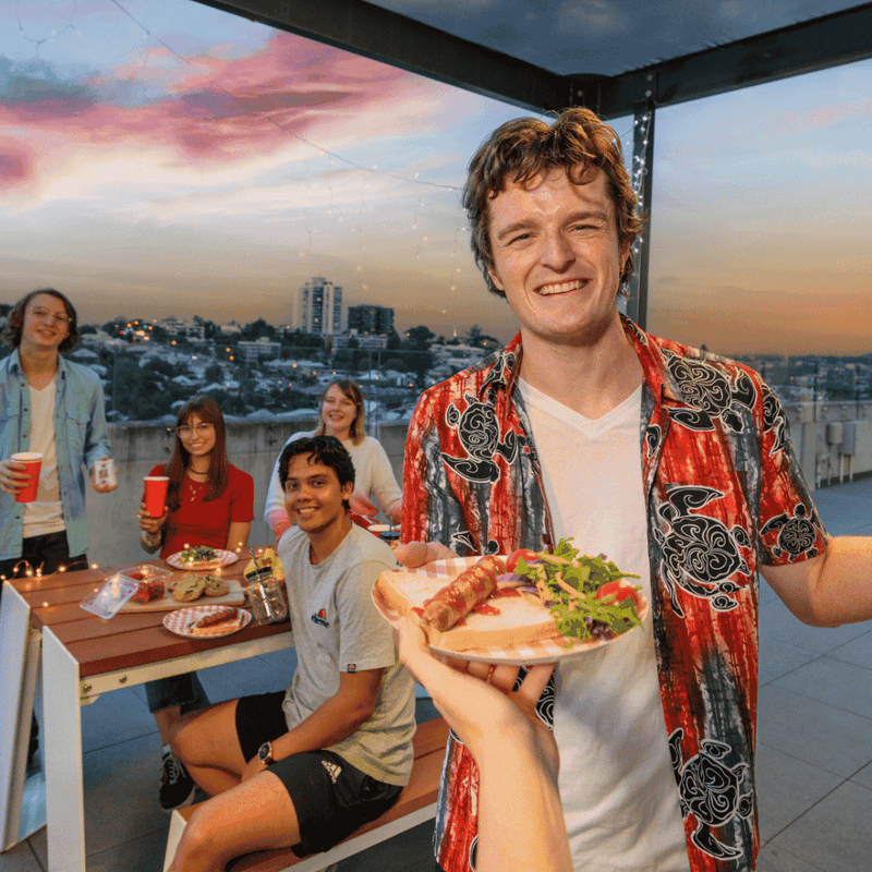 Young guests enjoying a rooftop barbecue gathering at sunset with city views at UniLodge South Bank