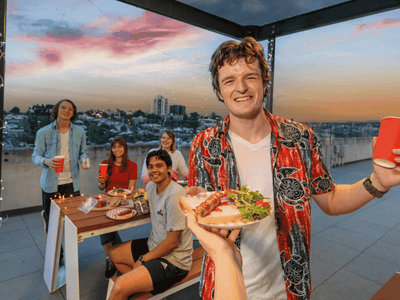 Young guests enjoying a rooftop barbecue gathering at sunset with city views at UniLodge South Bank